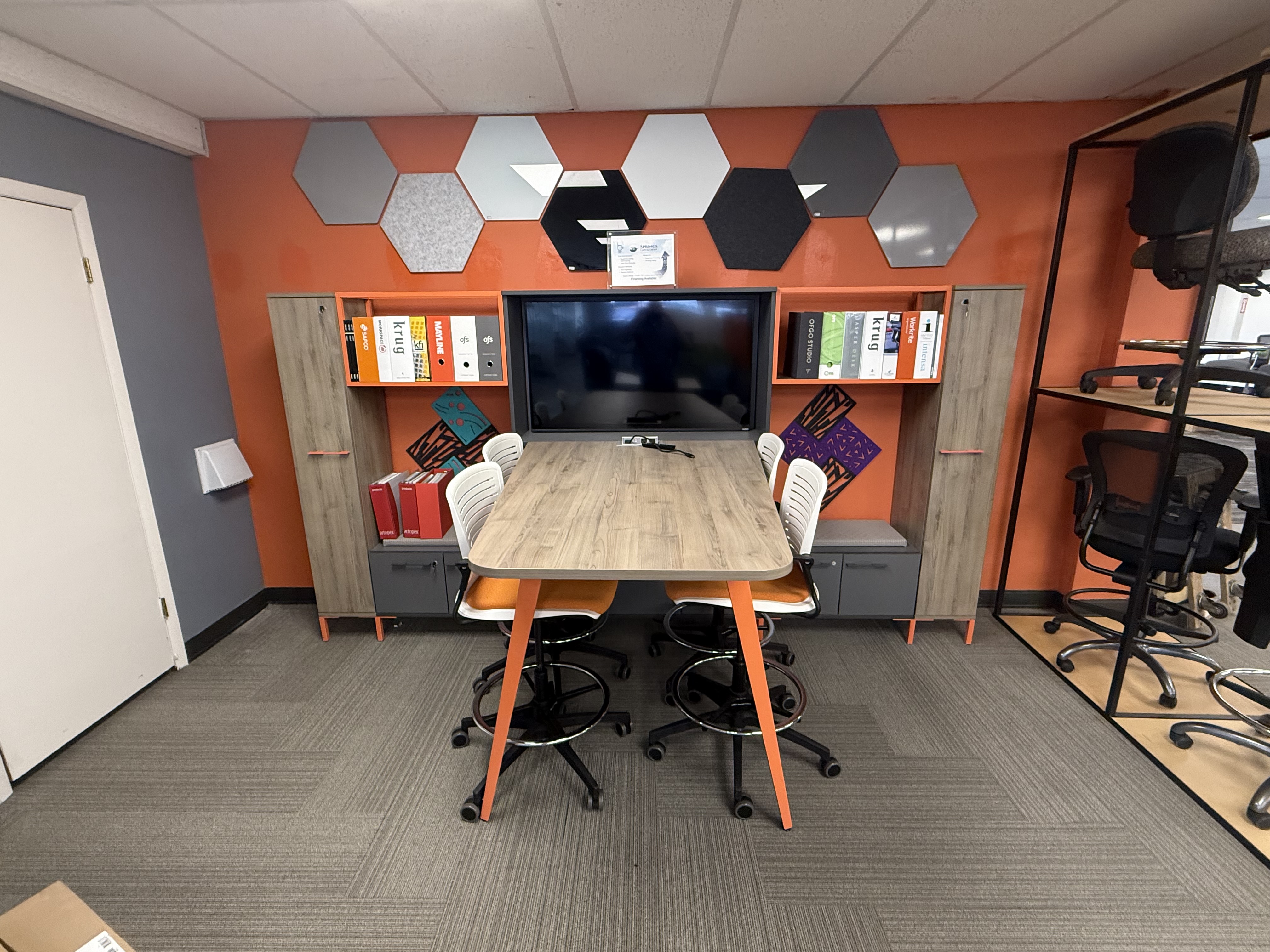 Collaboration space with conference table, orange accent wall, and hexagon acoustic panels