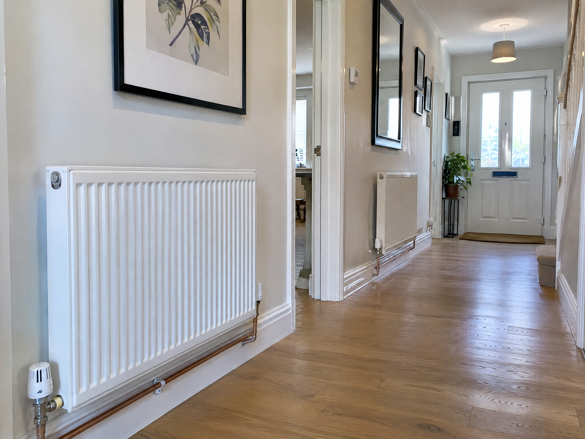 Row of modern panel radiators with thermostatic valves in a UK home hallway