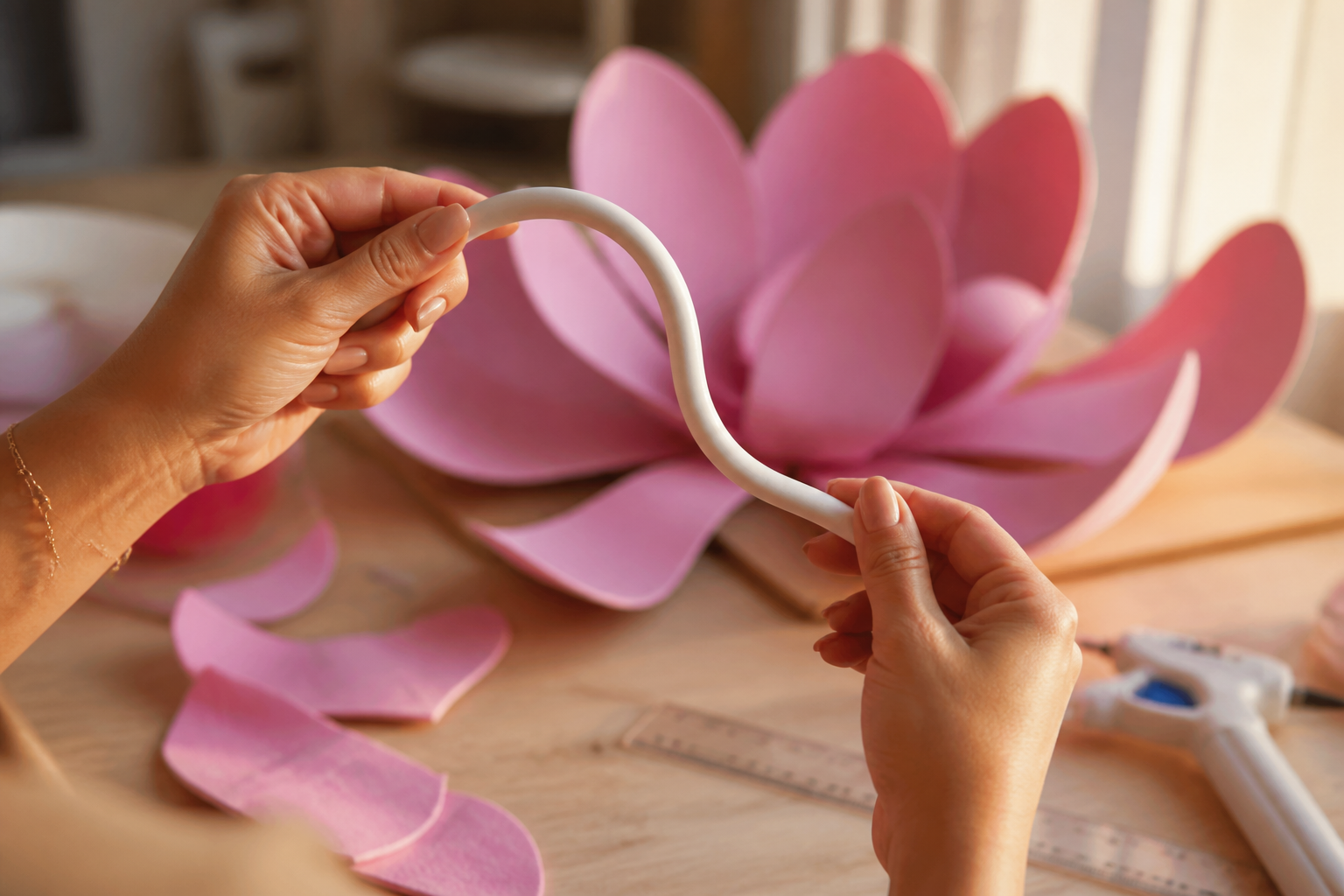 Hands bending a white PVC pipe into a graceful curved stem for a giant foam flower build