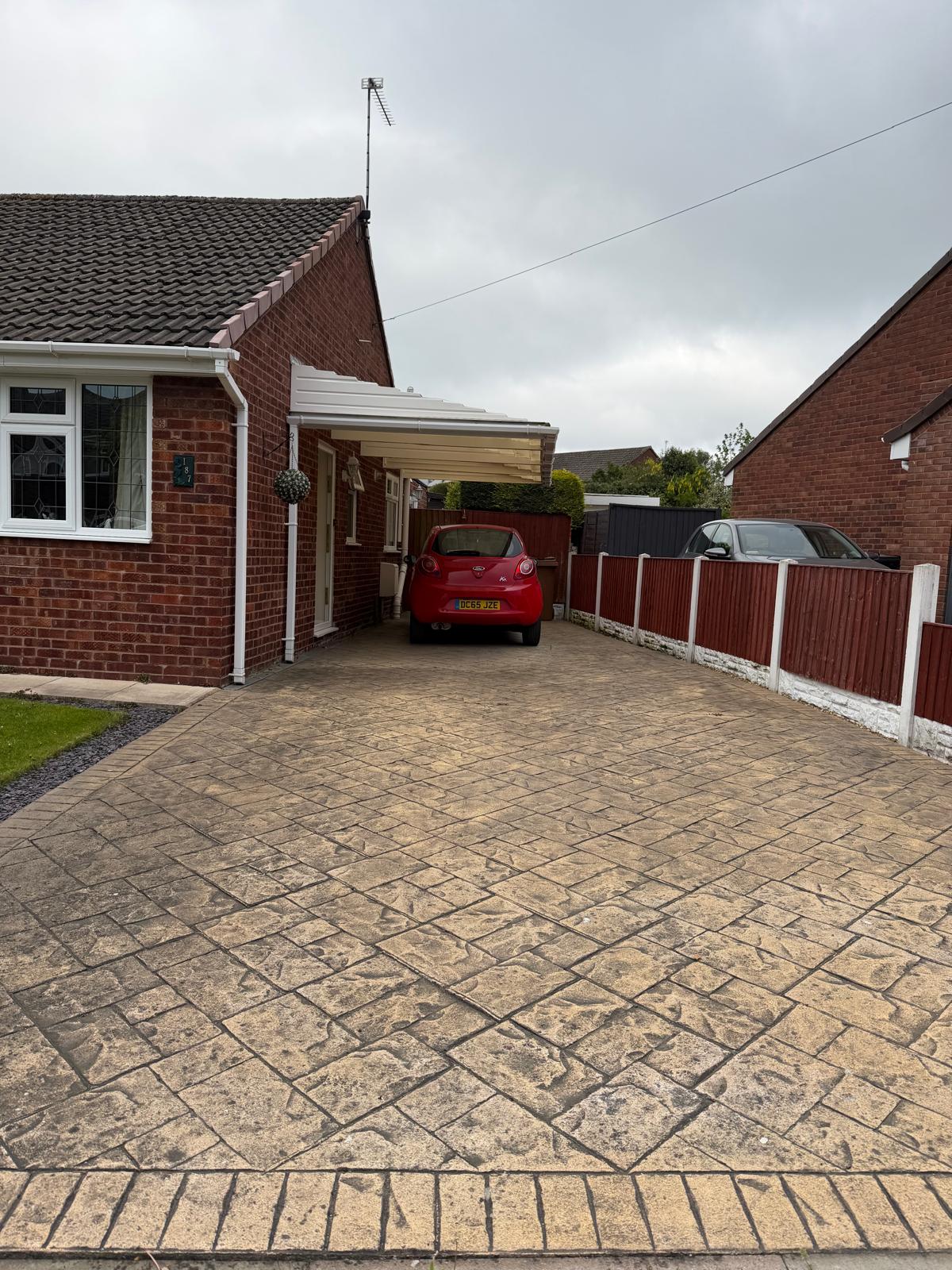Cleaned stamped concrete driveway with red car parked under carport