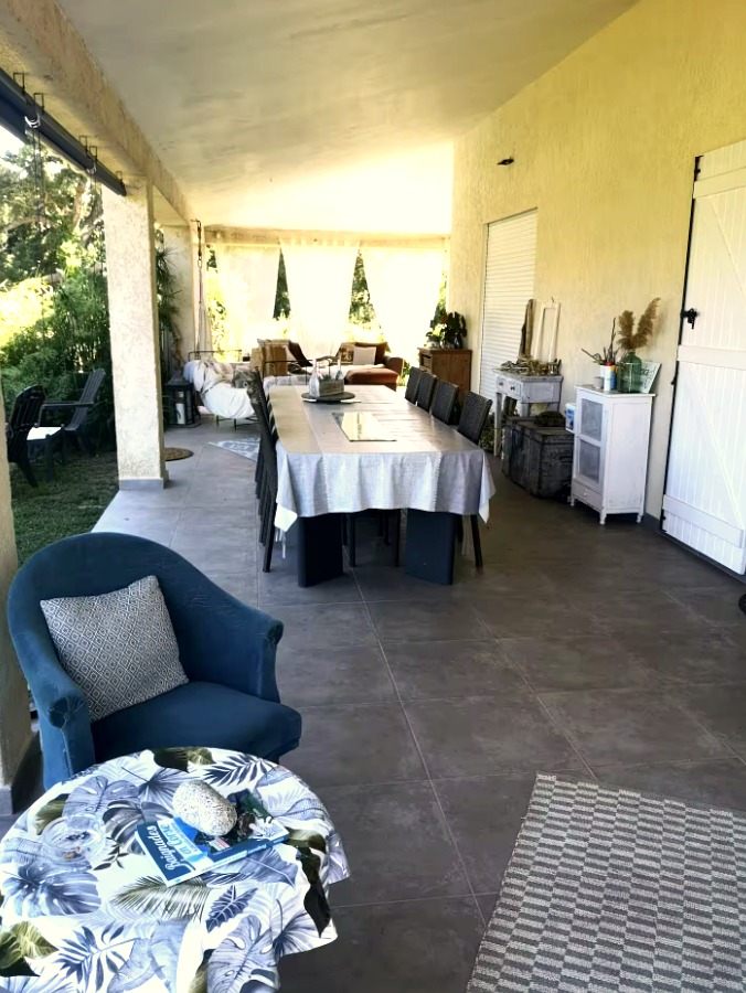 Grande terrasse couverte avec longue table et fauteuil bleu