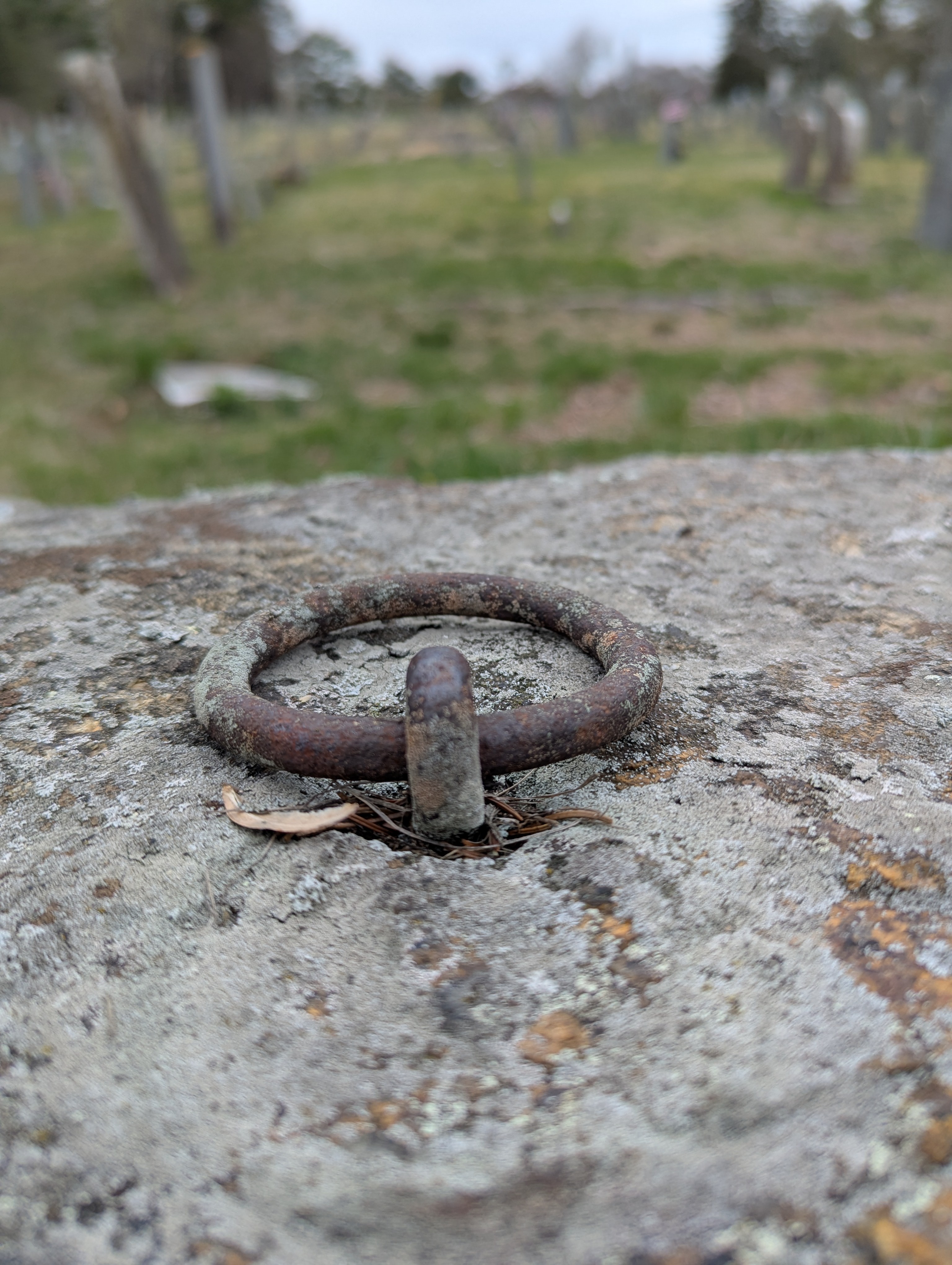 Close-up of the weathered iron hitching ring set into granite, showing centuries of rust and patina with the burying ground in the soft background