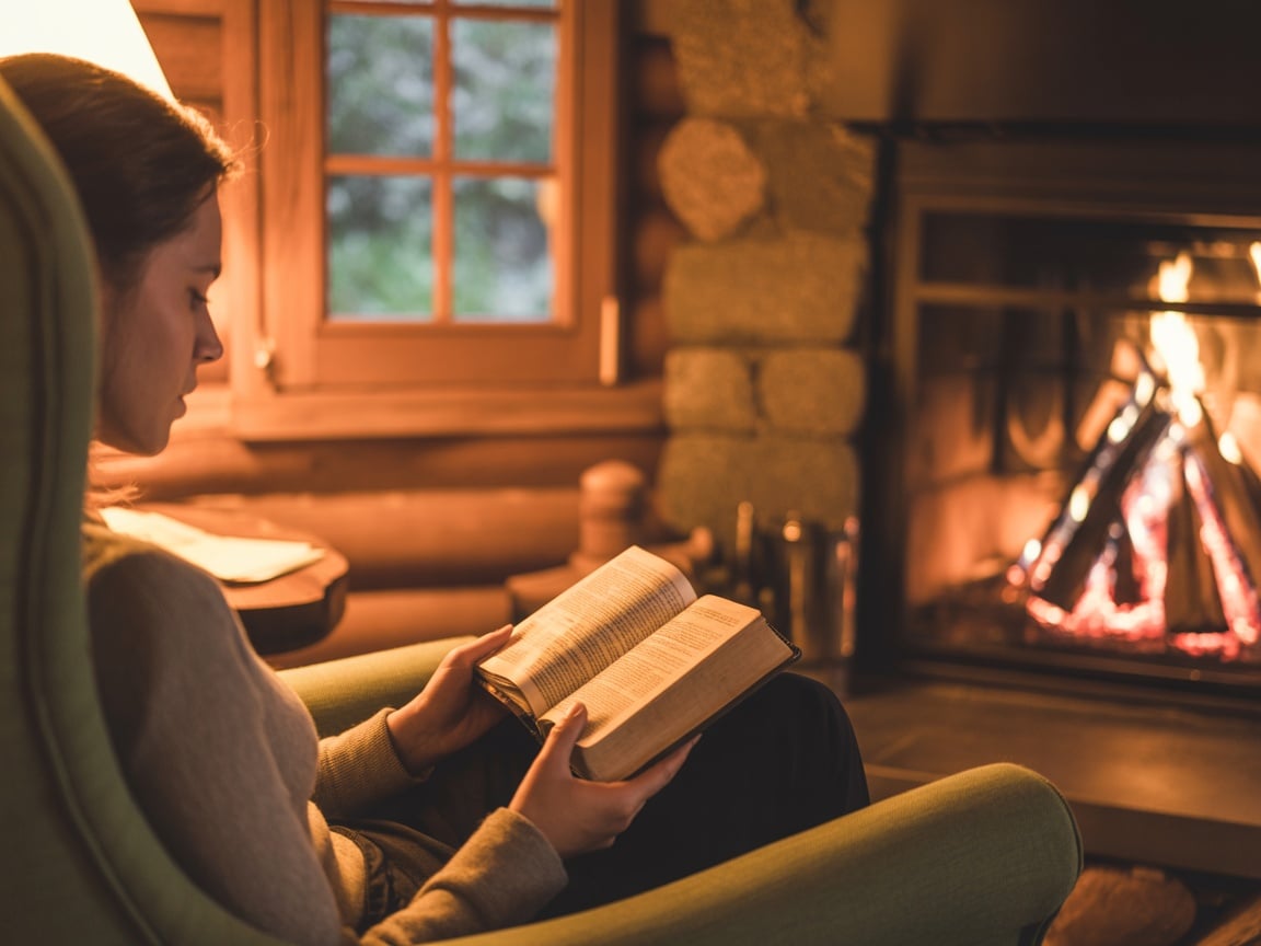 Person reading by a fireplace in a cozy cabin