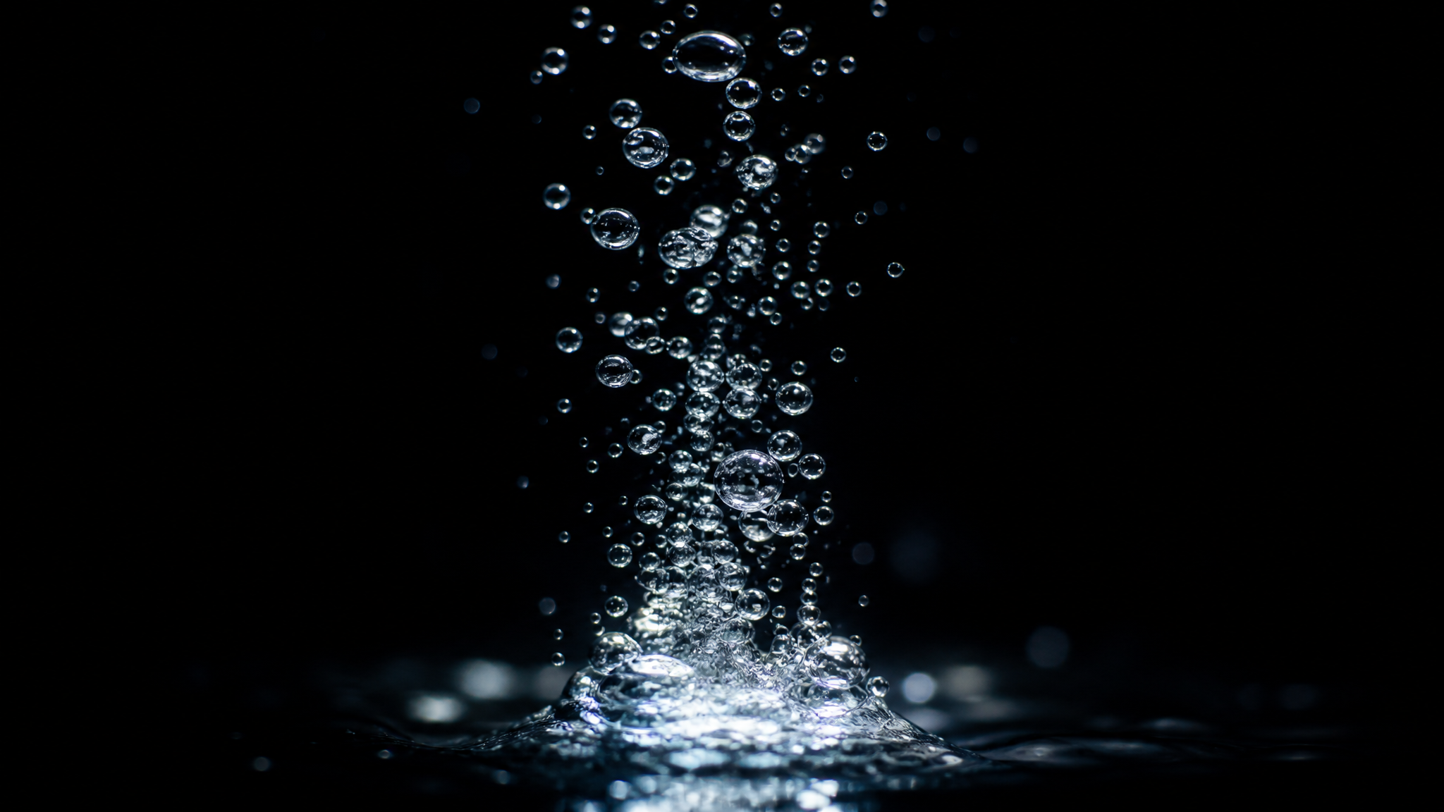 Fine air bubbles rising in a slow stream through clear water, lit from below.