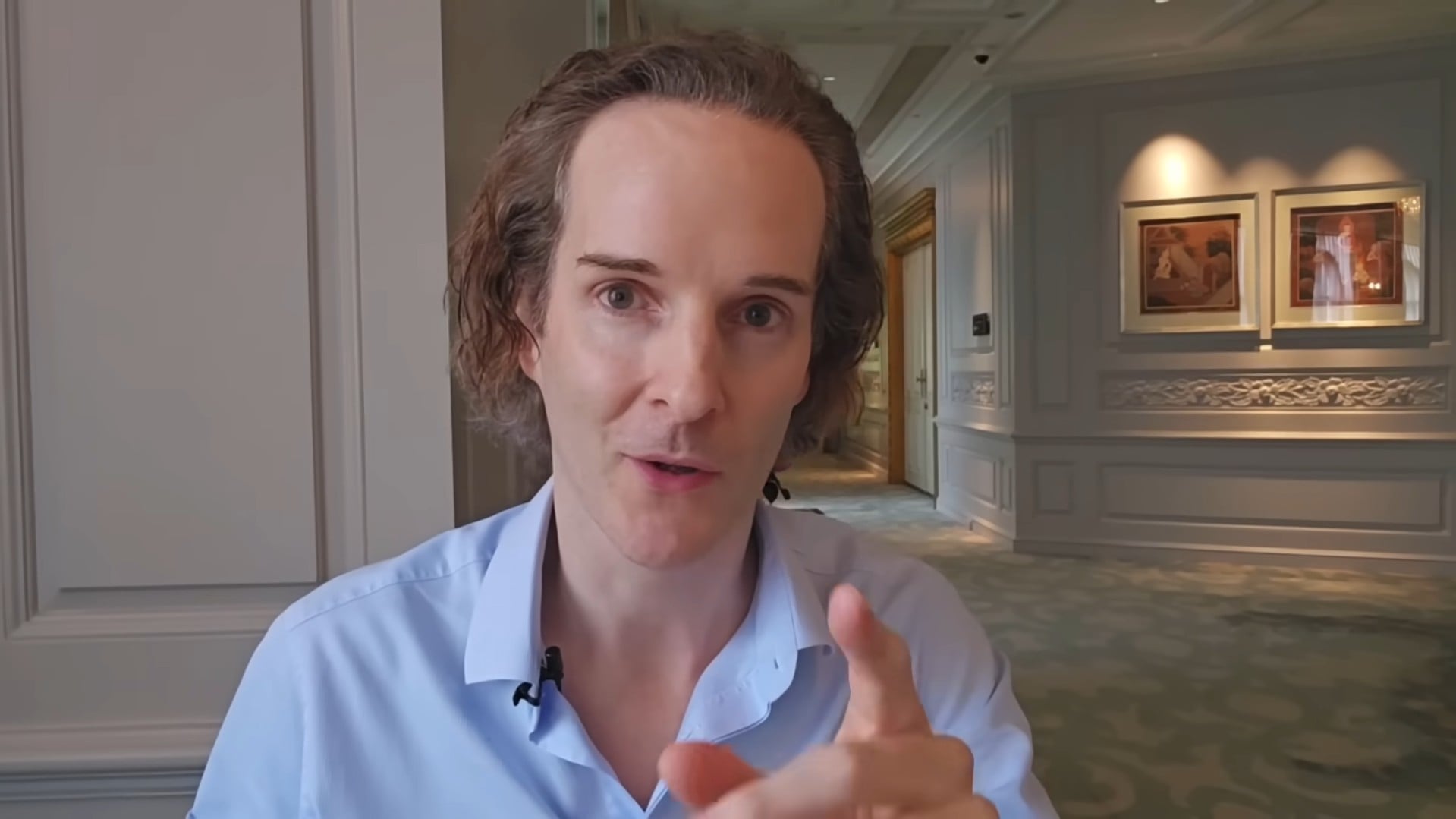 Felix Nikolas Prehn pointing towards the camera in a pale blue shirt in a corridor lined with framed pictures