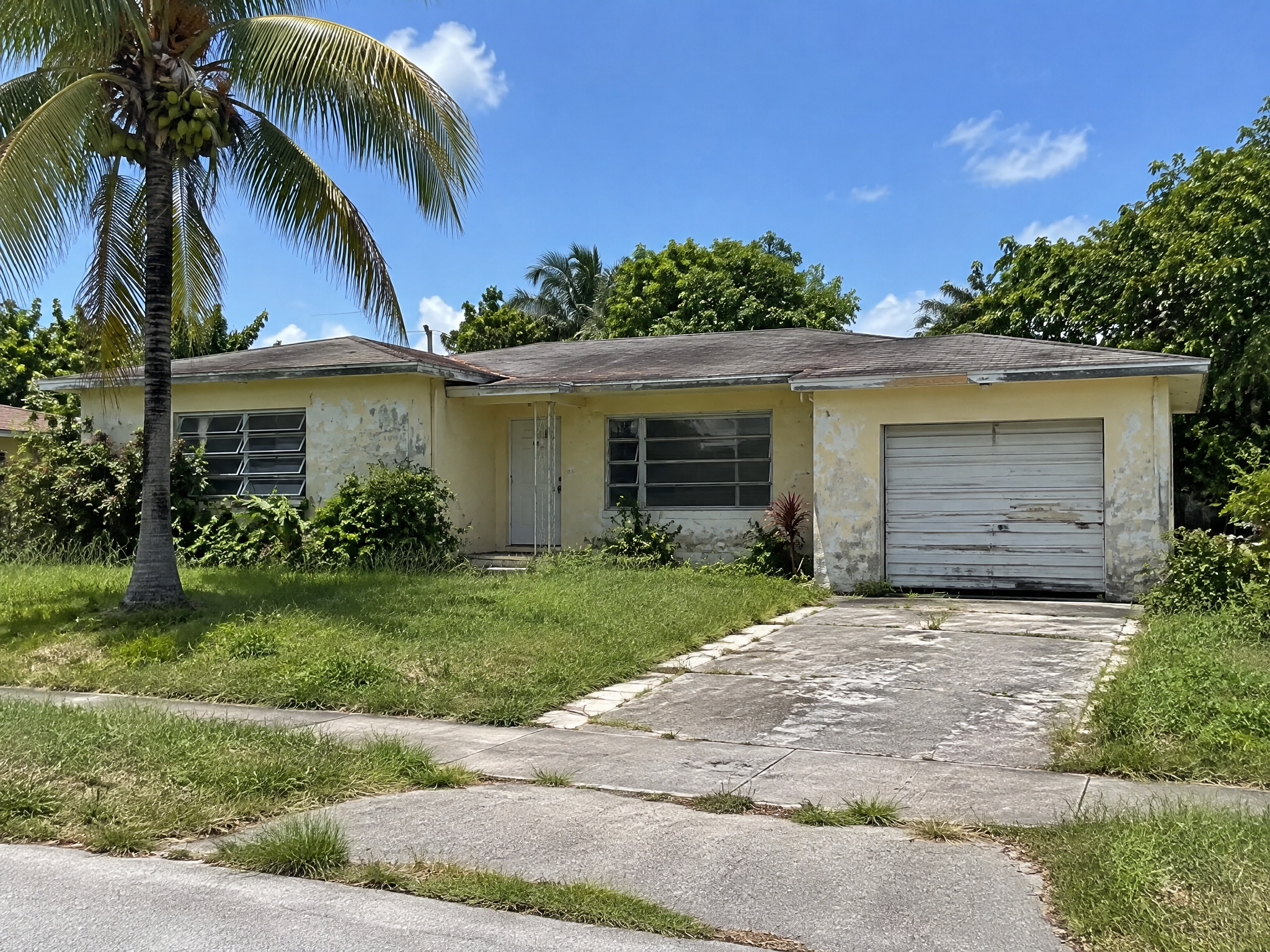 Dated Miami ranch house before renovation with peeling paint and jalousie windows