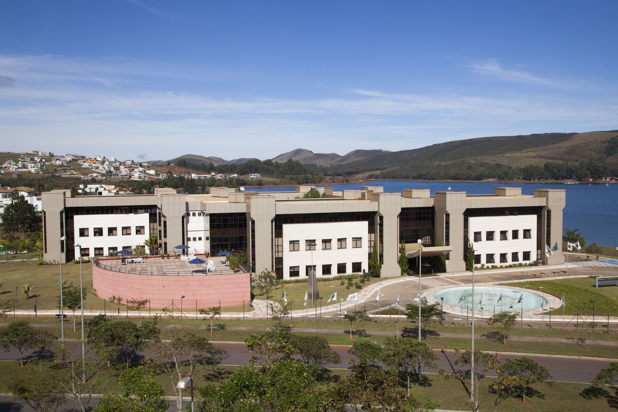Vista aérea de um campus da Fundação Dom Cabral, com edifícios brancos, jardins e um lago ao fundo