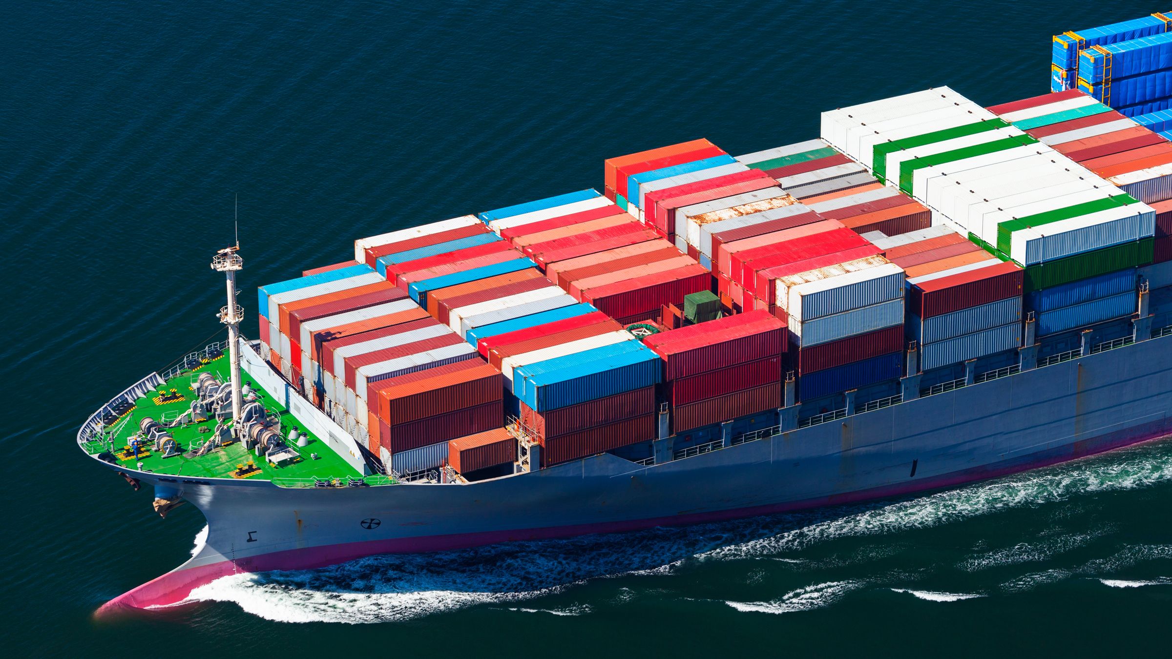 Large cargo container ship loaded with shipping containers navigating ocean waters, representing international trade and global supply chain operations affected by carbon border adjustment mechanisms