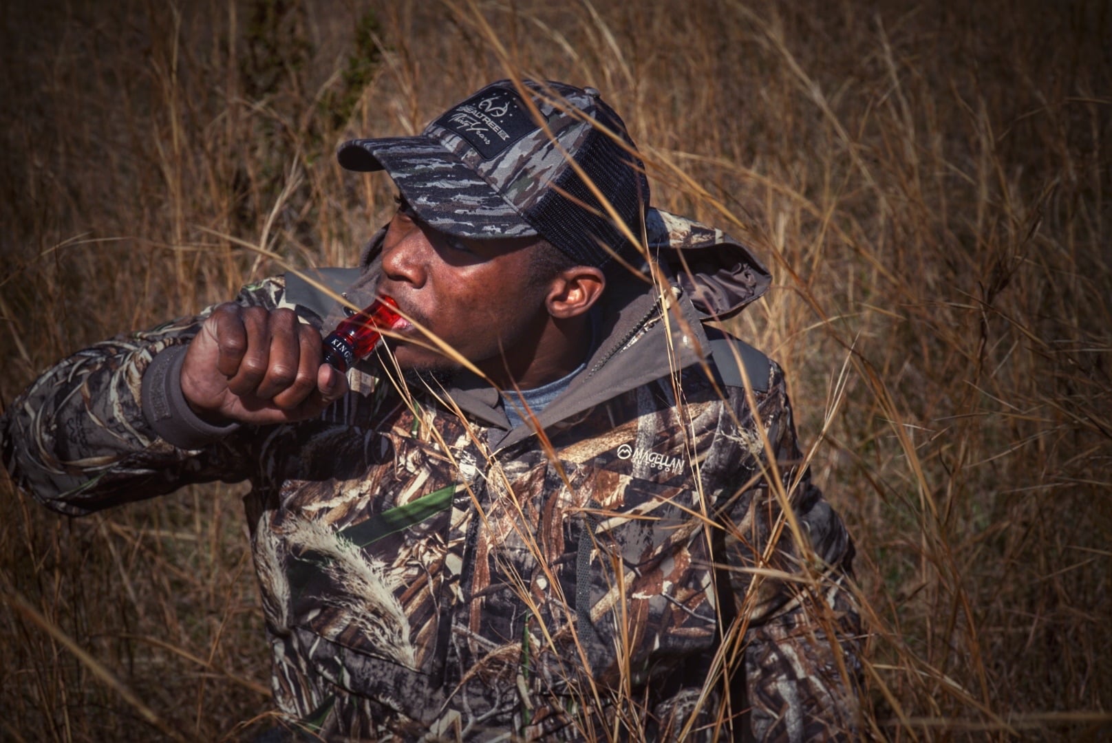 Joshua in full camo using a game call concealed in tall grass