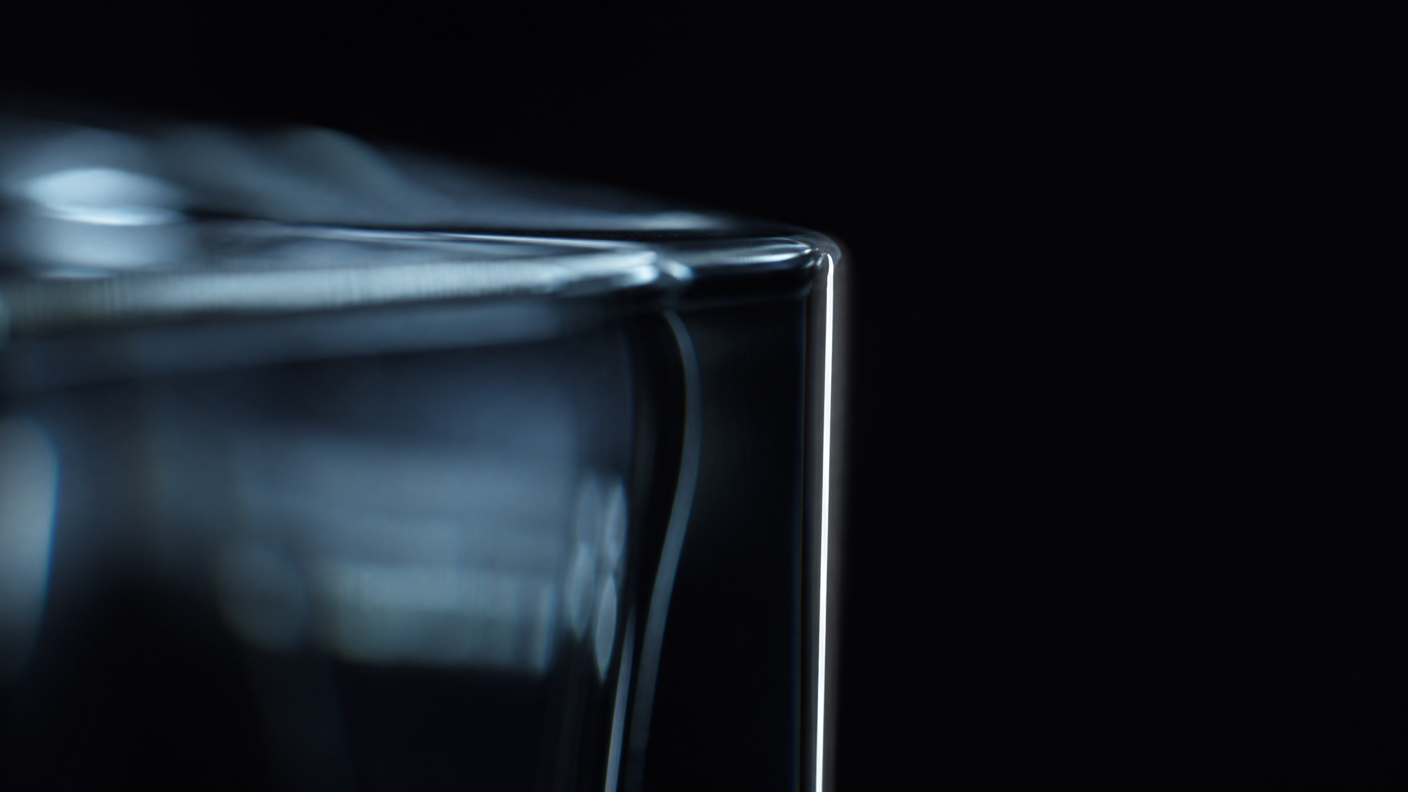 The corner edge of thick clear glass catching a thin sliver of white light.