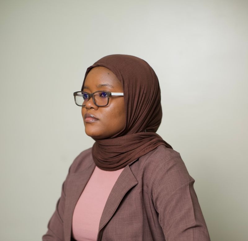 Professional African Muslim woman wearing a brown hijab glasses and a mauve blazer looking thoughtfully to the side in a studio portrait