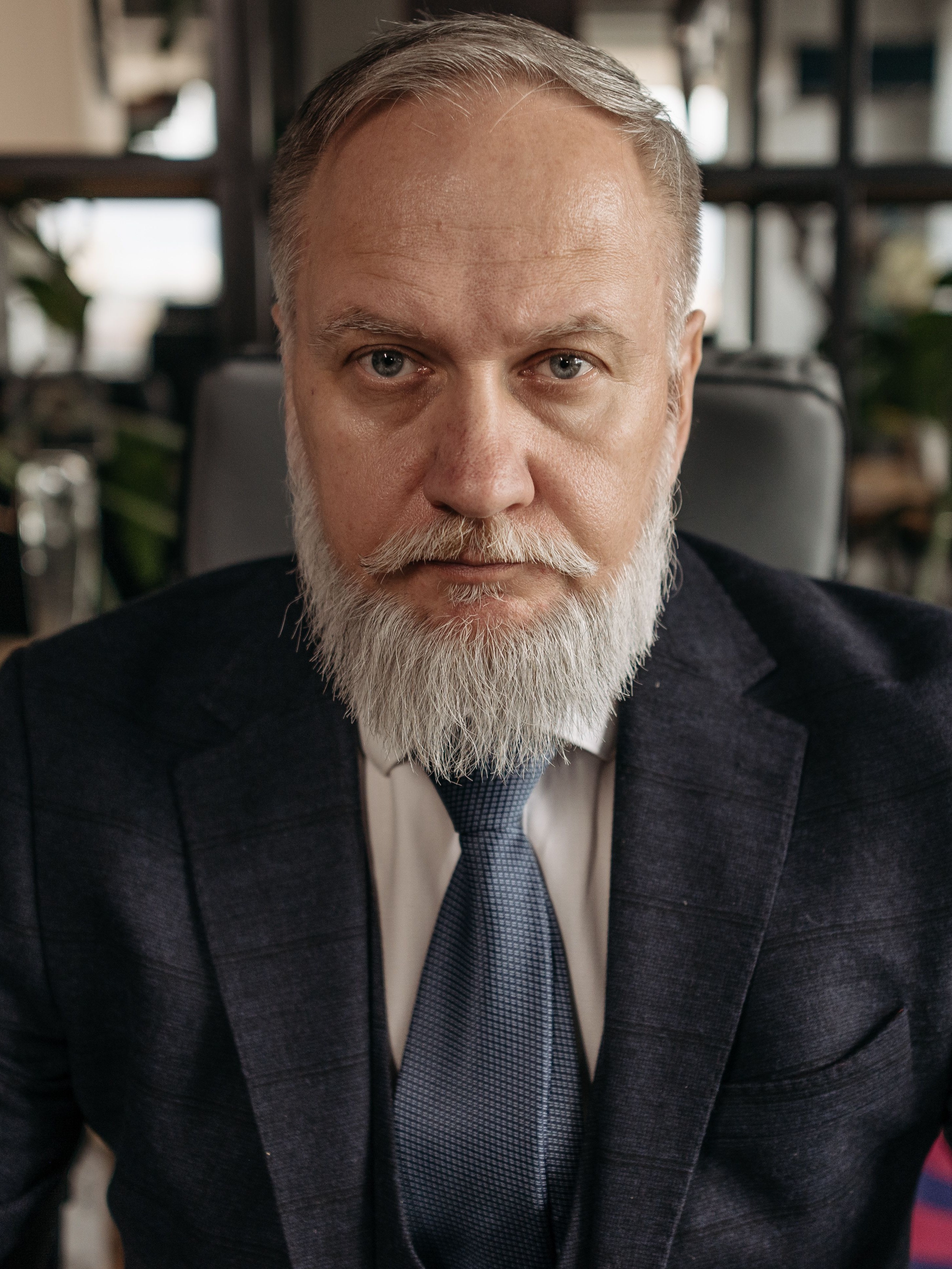 Professional portrait of an older bearded man in a navy suit serving as a veterans benefits advocate