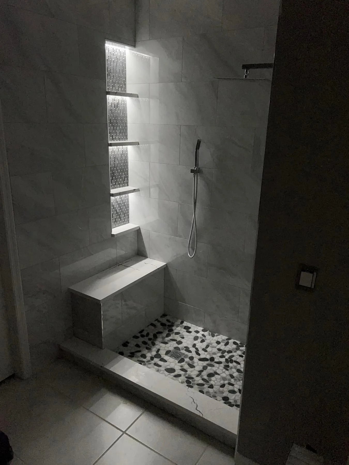 Modern walk-in shower with gray marble tiles, built-in shelves, and pebble stone floor